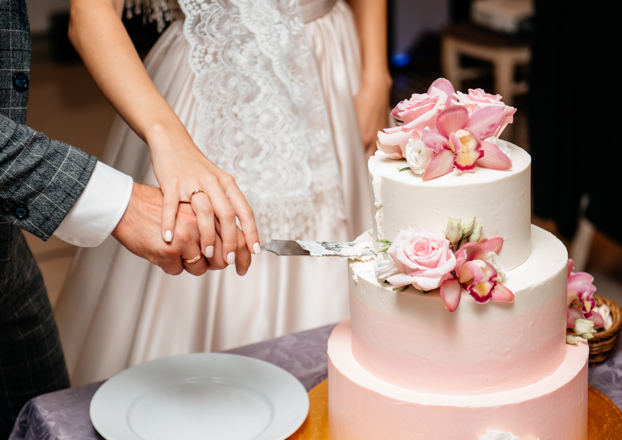 Braut und Bräutigam schneiden die Hochzeitstorte an, die Hand der Braut liegt dabei auf der des Mannes