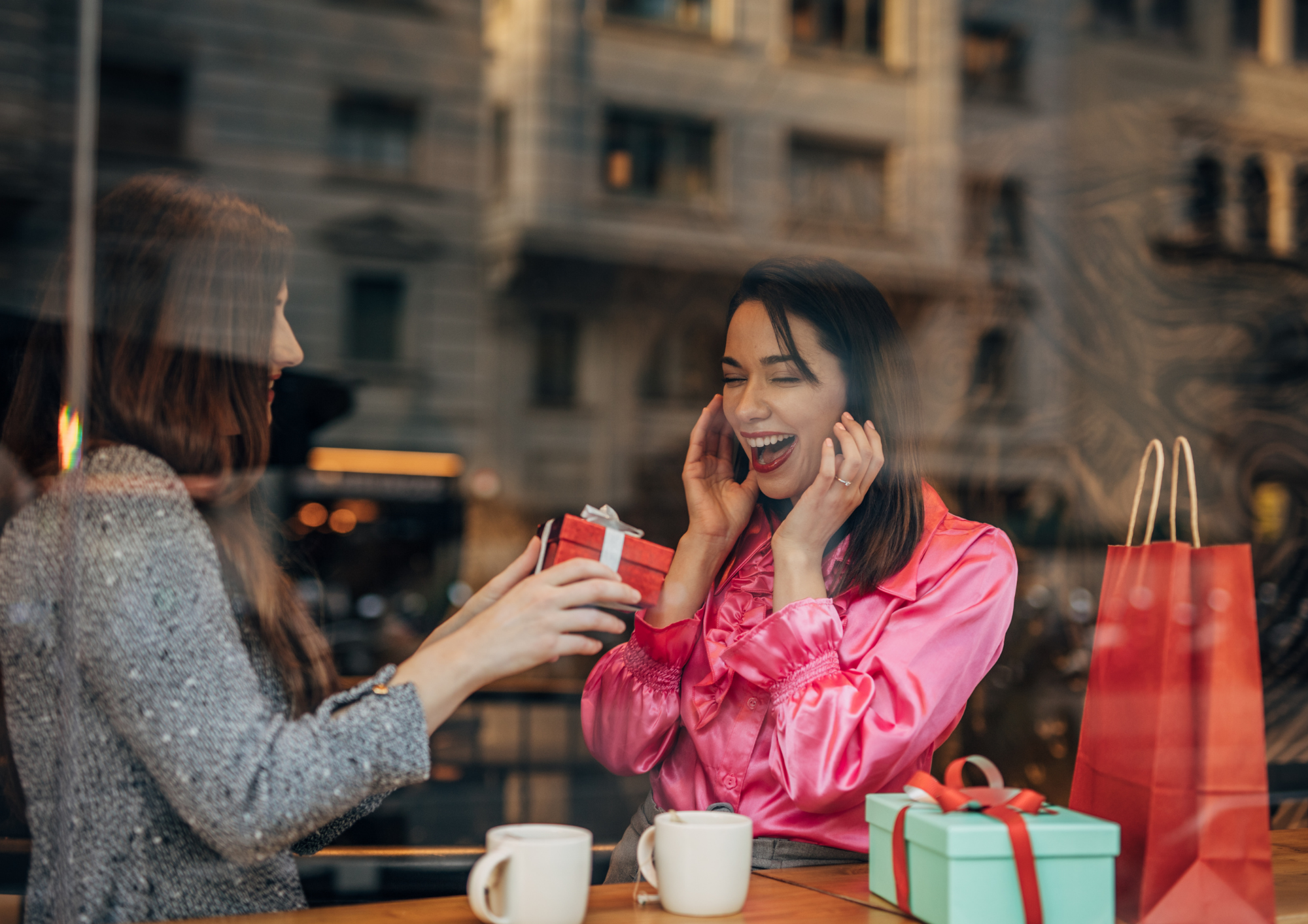 Zukünftige Braut übergibt der Trauzeugin ein Geschenk in einem Café. Die Trauzeugin ist glücklich überrascht