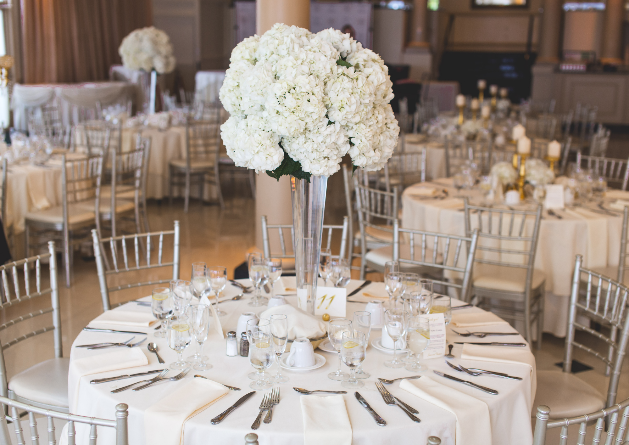 Hochzeitstisch mit minimalistischer klassischer Dekoration bestehend aus weißen Hortensien und weißer Tischdecke in einem Festsaal