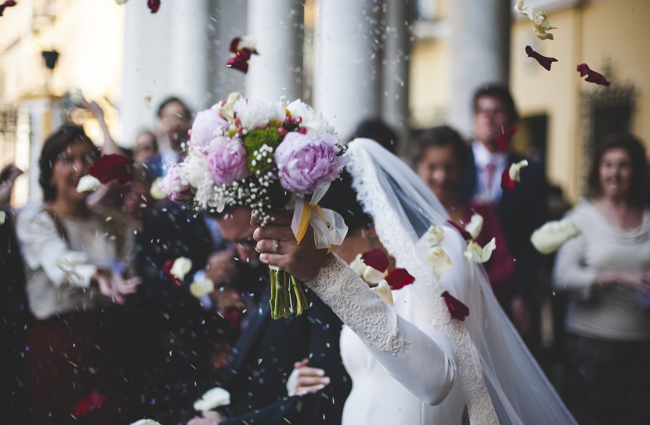 Hochzeitspaar läuft aus der standesamtlichen Trauung und wird von ihren Gästen mit Rosenblüten und Reis begrüßt