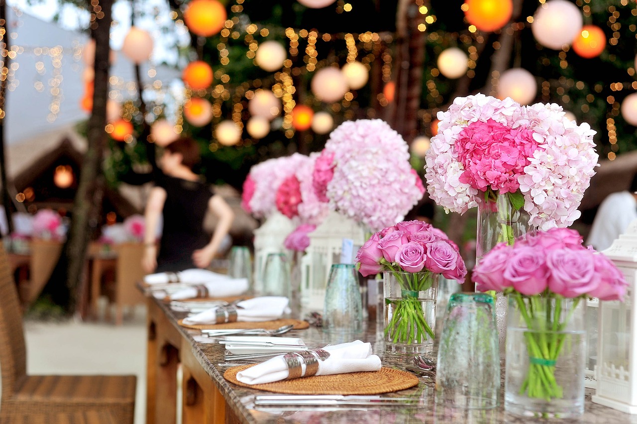 Schöner Hochzeitstisch mit rosanen Blumen in Gläschen und Lichterketten für die romantische Note